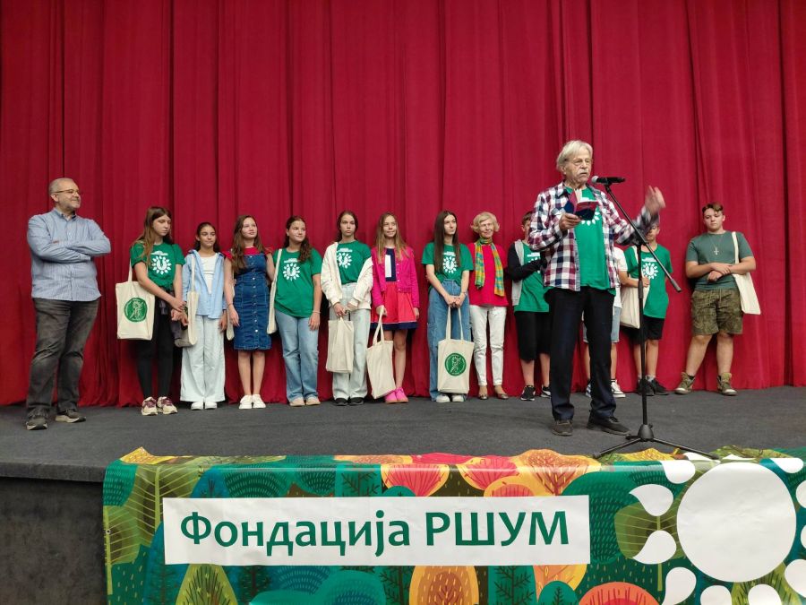 Приредба Академије ,,Сарадници сунца" deca na sceni ispred njih stoji odrastao covek i recituje