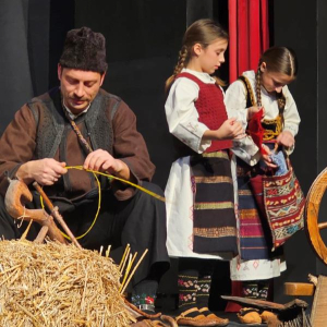 muskarac plete korpu u tradicionalnoj nosnji, dve devojcice stoje pored