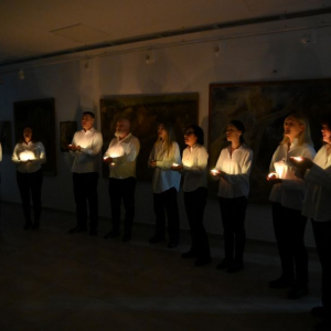 ljudi pevaju u mraku, drzeci svece