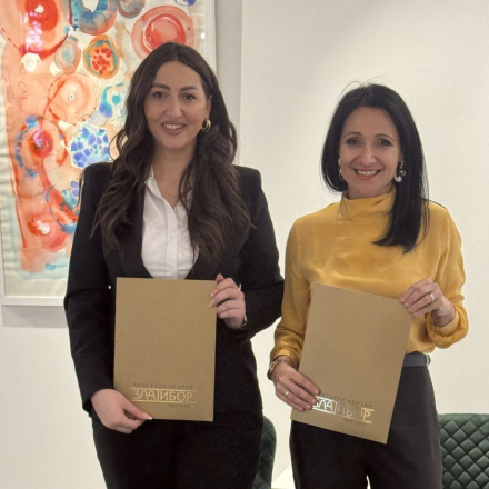 dve zene stoje i drze fascikle ispred sebe